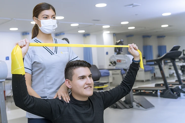 Profesional de la salud supervisando a un paciente durante una sesión de rehabilitación física con una banda elástica de resistencia.